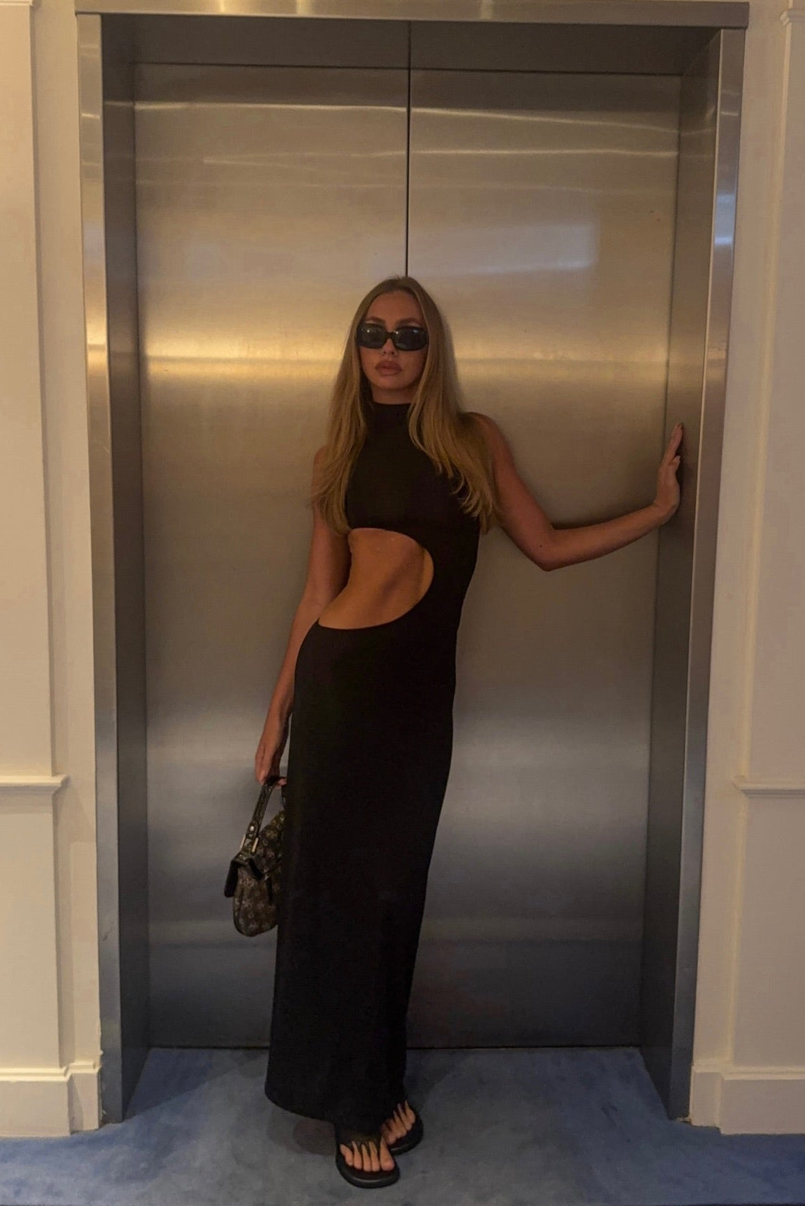Woman in a black dress standing in front of an elevator.