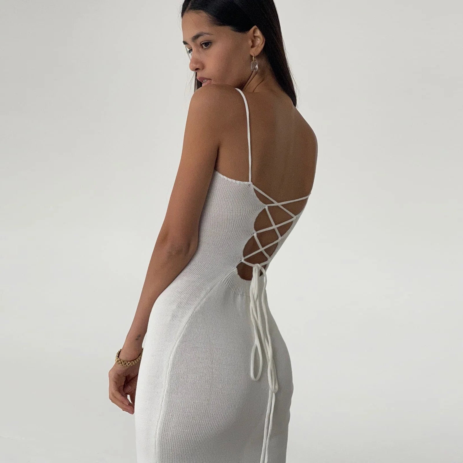 Woman wearing a white dress with criss-cross back design on a plain background