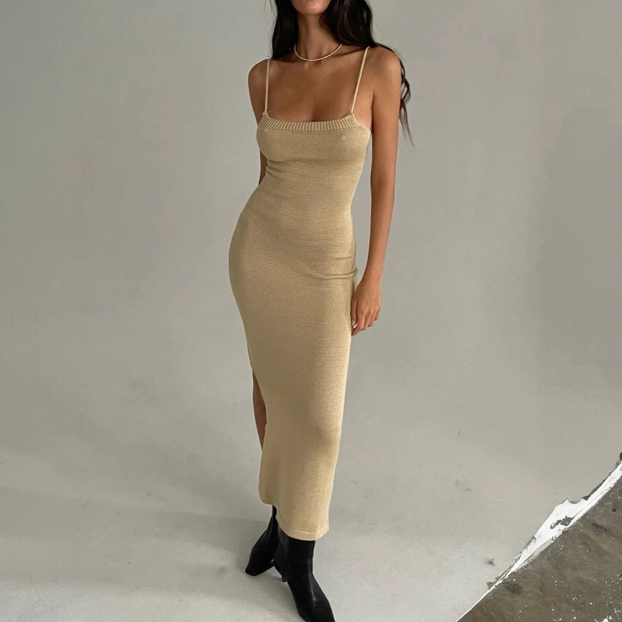 Woman wearing a beige dress with a slit on a plain background