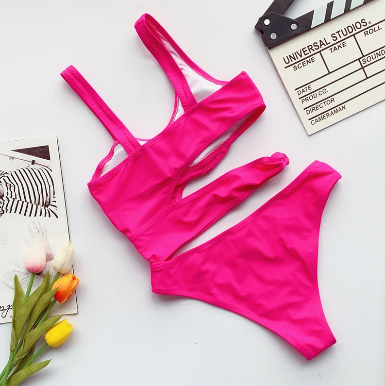 Pink bikini set on a white surface with flowers and a clapperboard.