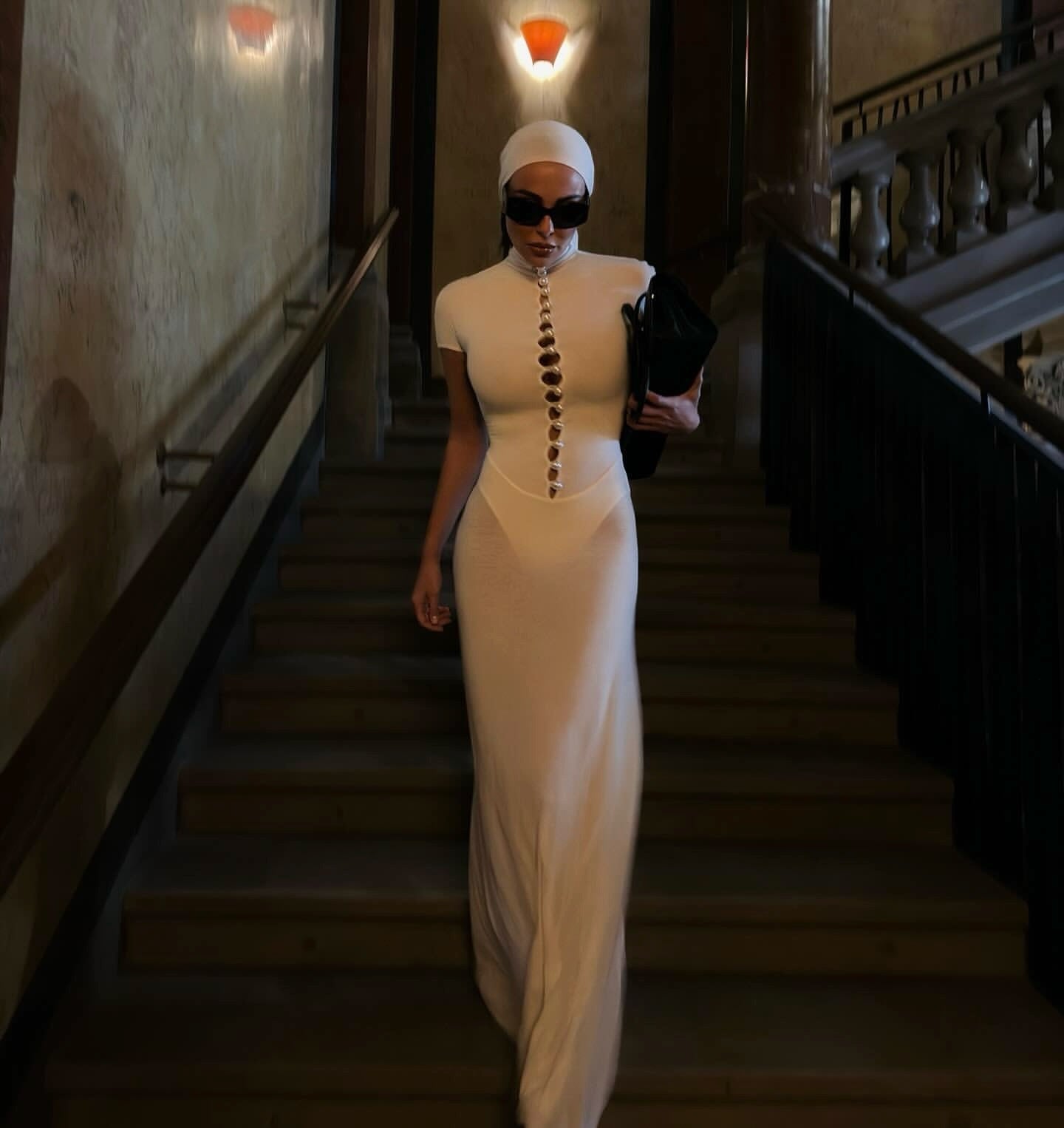 Woman in a white dress with a headscarf walking down a dimly lit staircase.