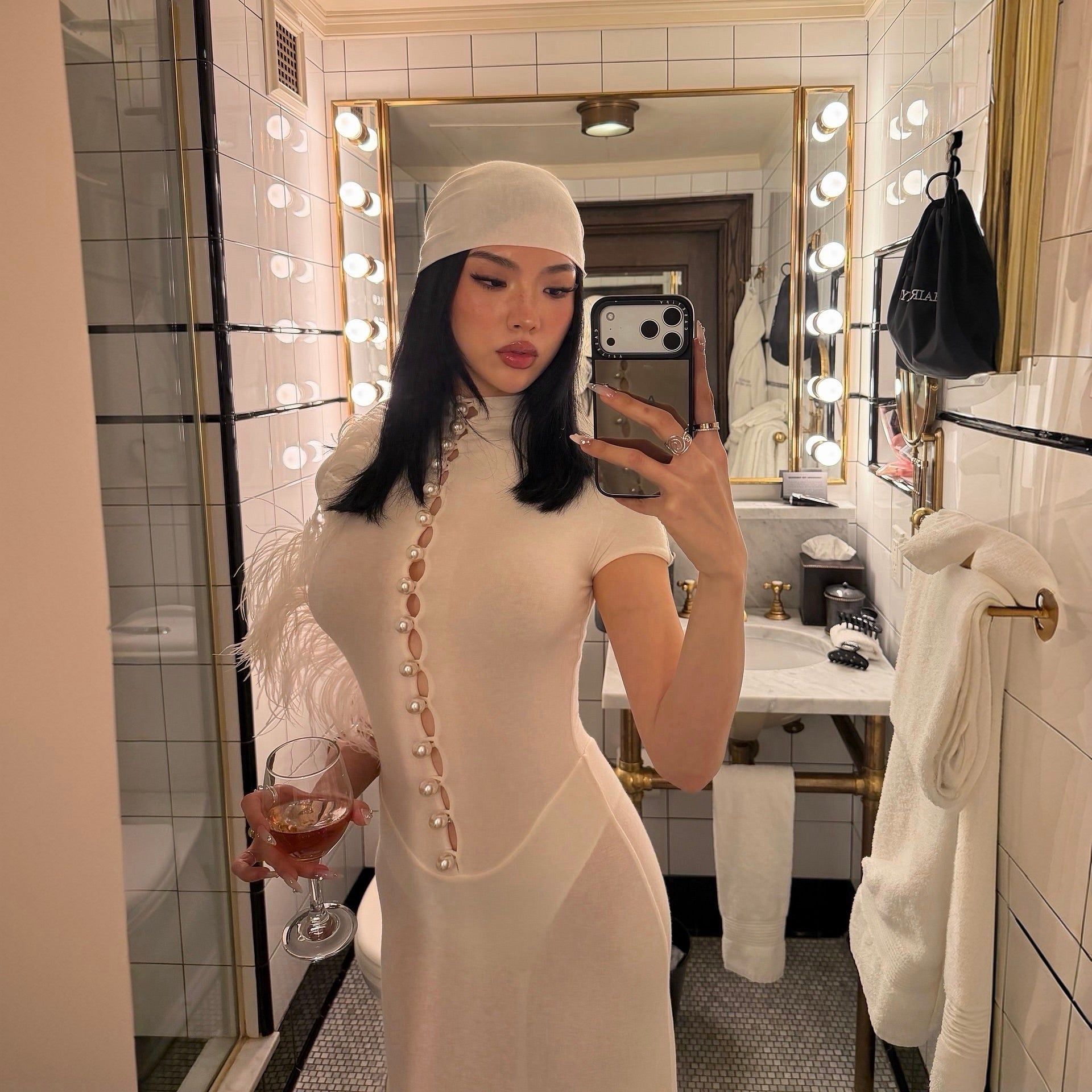 Woman in a white dress taking a mirror selfie in a bathroom.
