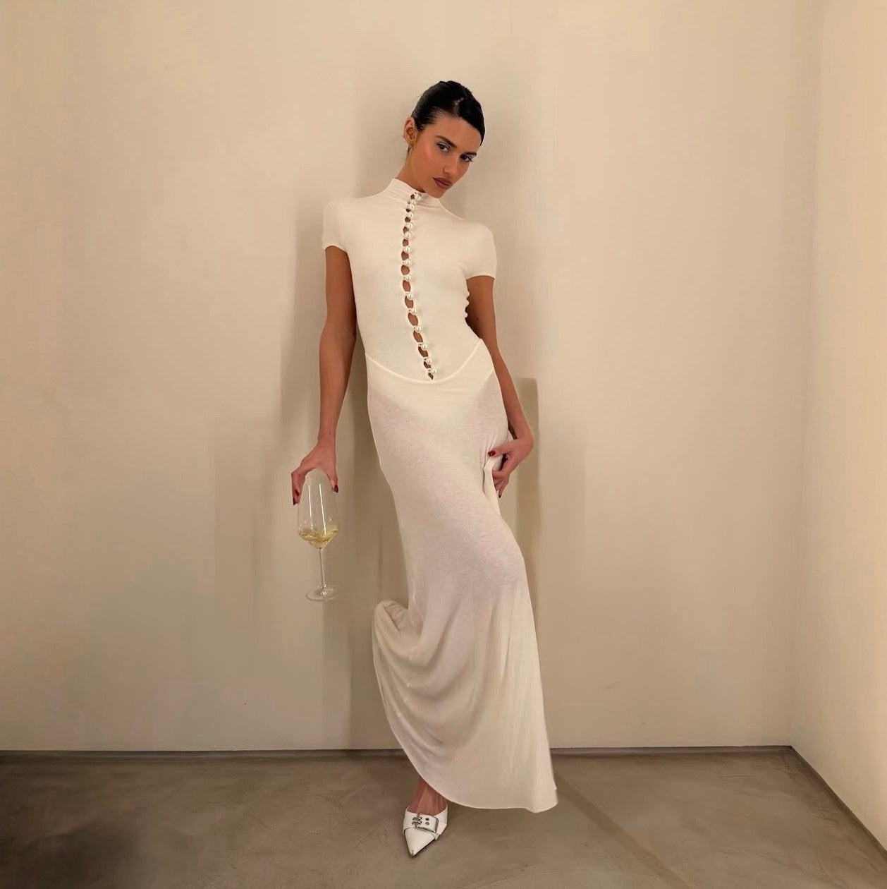 Woman in a white evening gown holding a glass against a plain background