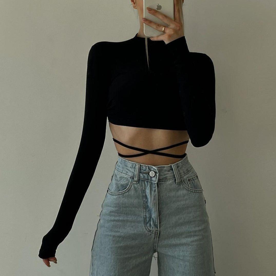 Person wearing a black long-sleeve crop top and light blue jeans against a plain background
