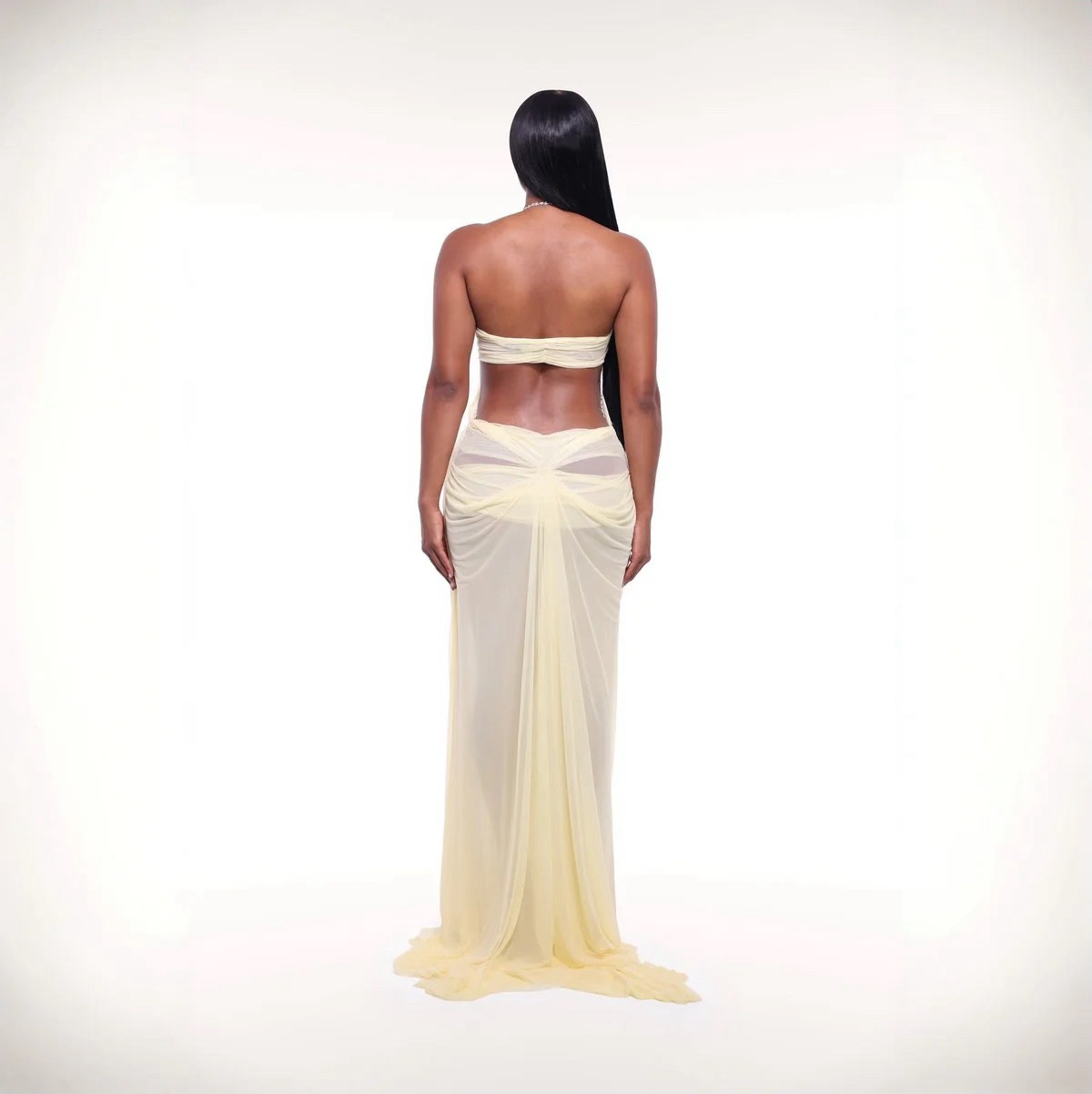 Woman wearing a strapless, sheer yellow gown on a white background