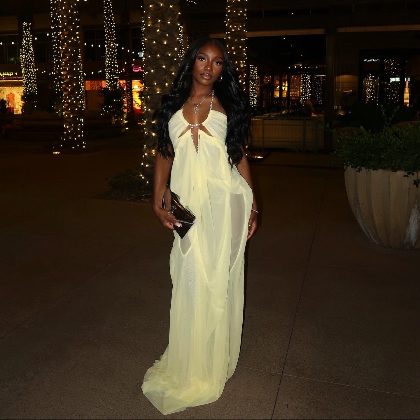 Woman in a white dress standing outdoors at night with decorated trees in the background