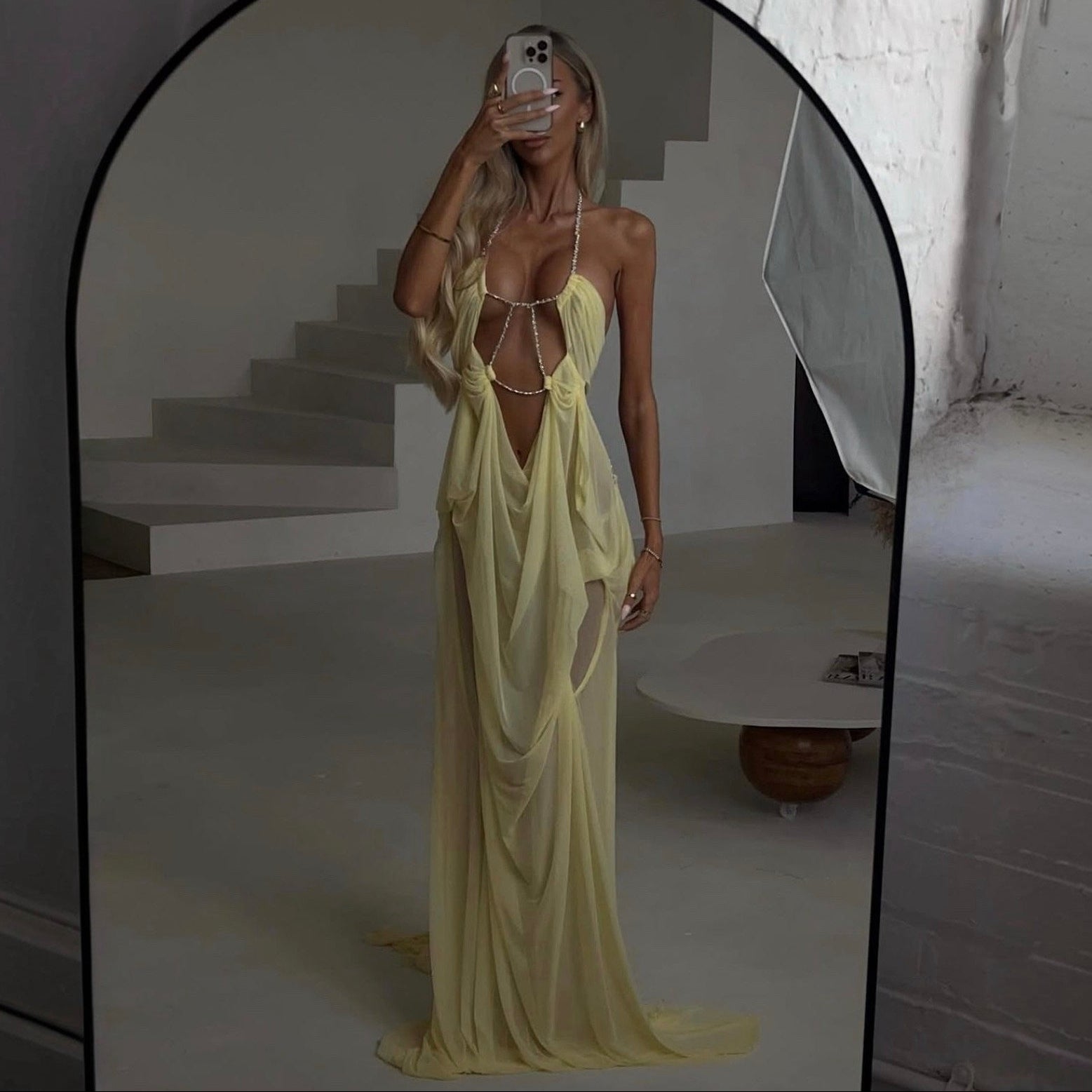 Woman in a yellow dress standing in front of a mirror in a minimalistic room.