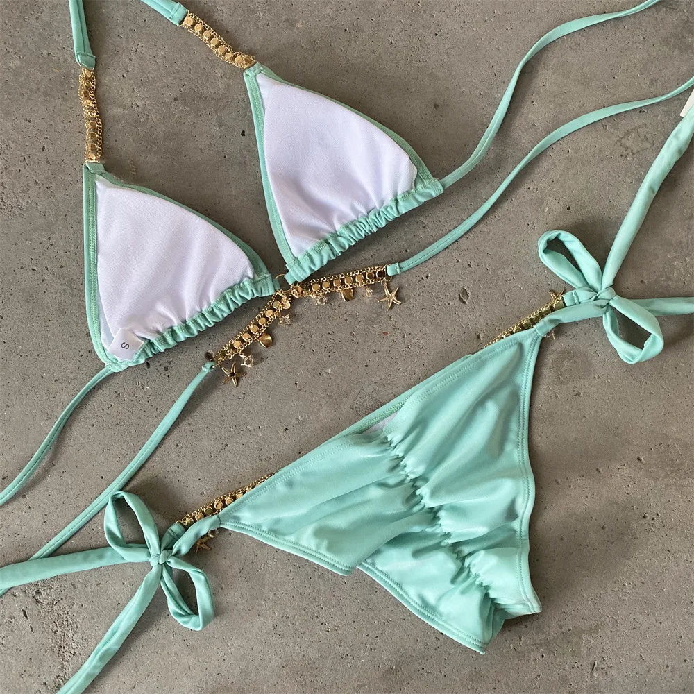 Mint green bikini set with gold accents on a concrete surface