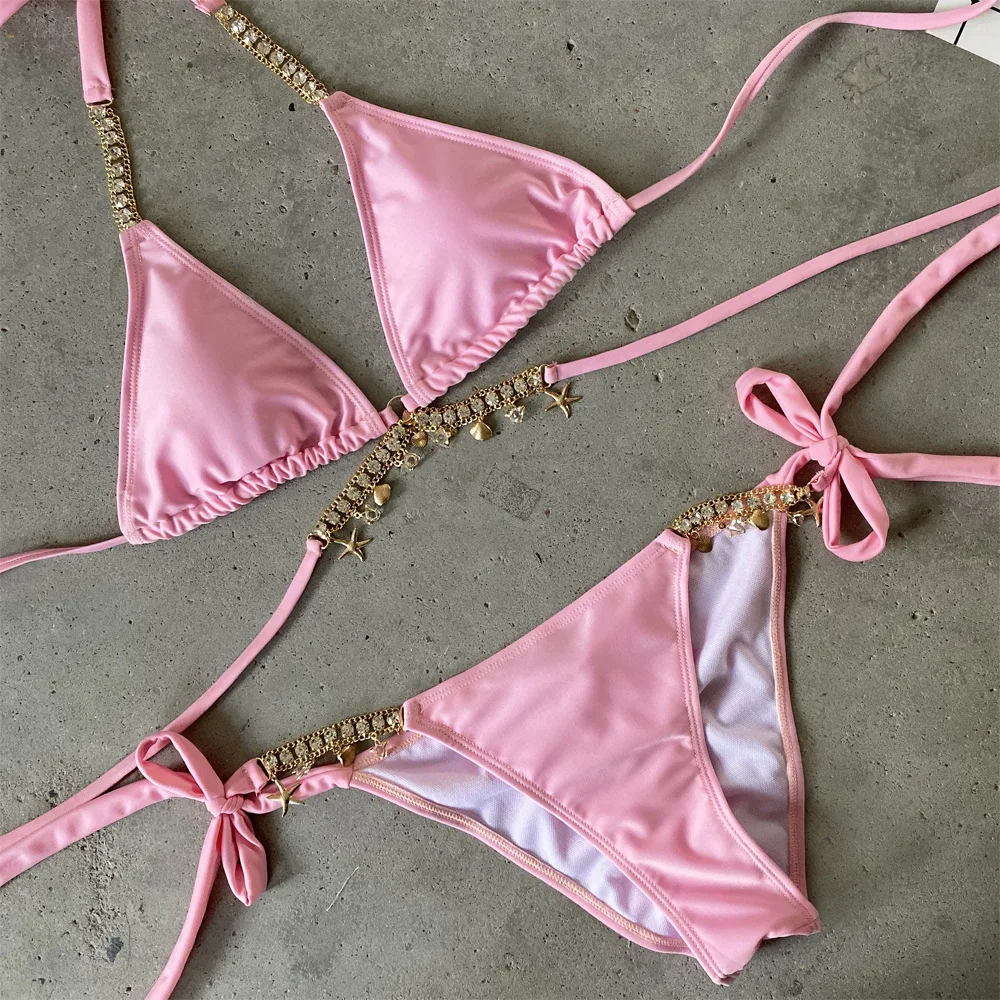Pink bikini set with gold accents on a concrete surface