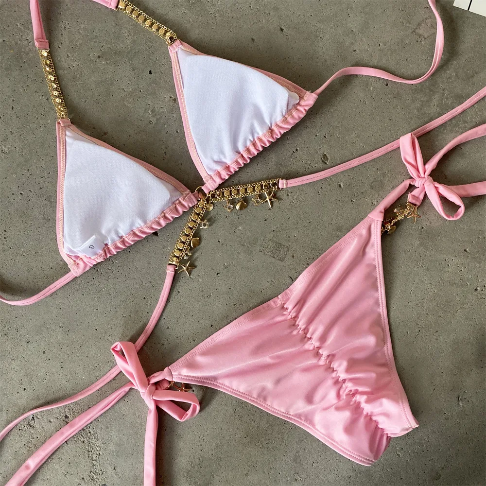 Pink bikini set with gold accents on a concrete surface