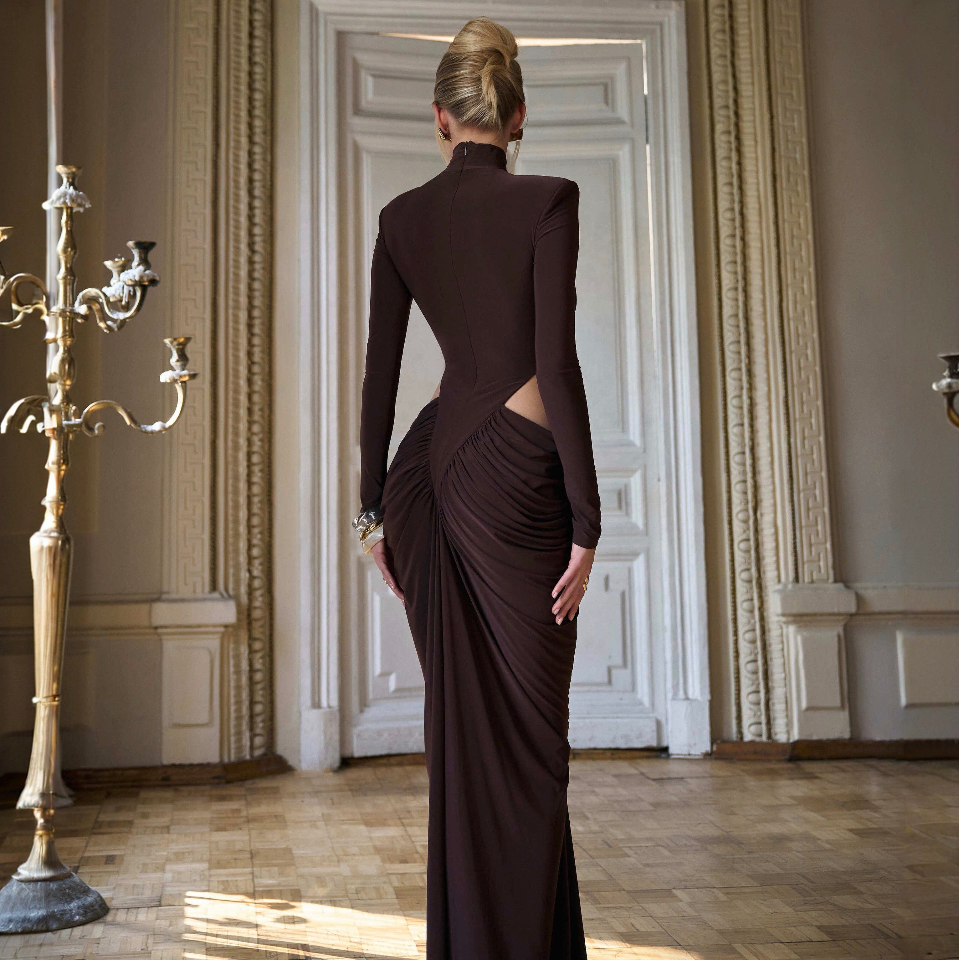 Woman in a dark brown evening gown with an open back in an elegant room.