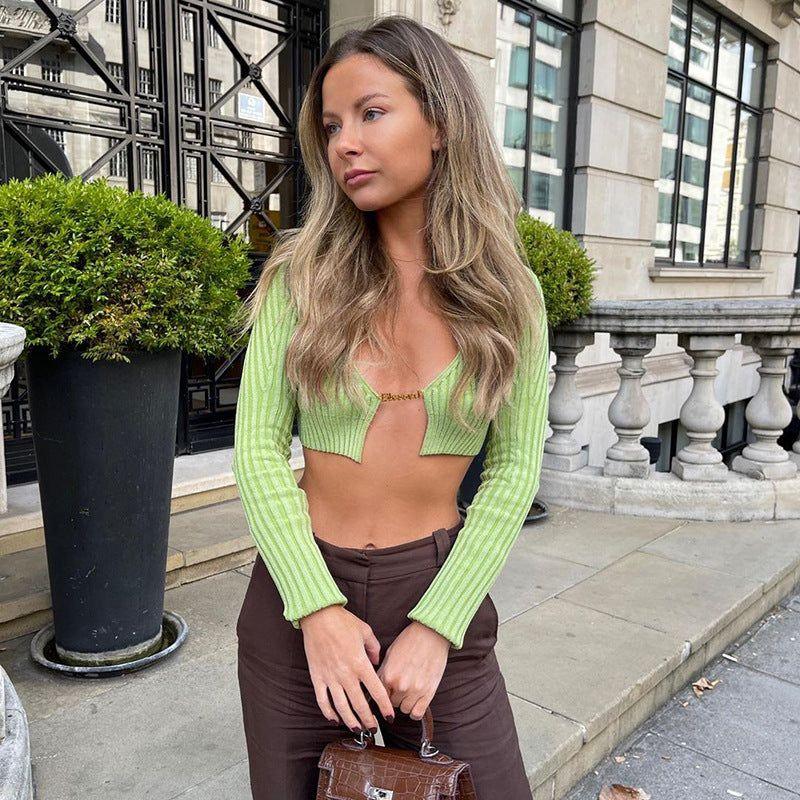 Woman wearing a green cropped cardigan and brown pants standing on a city street.