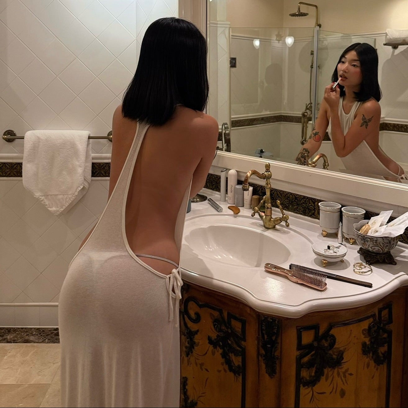 Woman in a white dress standing in front of a bathroom mirror, partially unclothed.