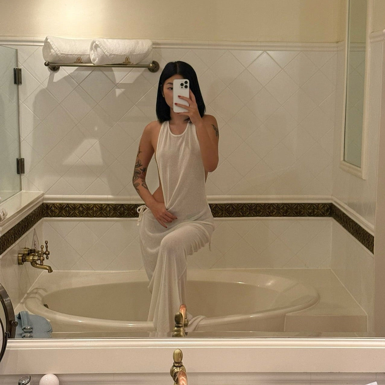 Person taking a mirror selfie in a bathroom wearing a white dress.