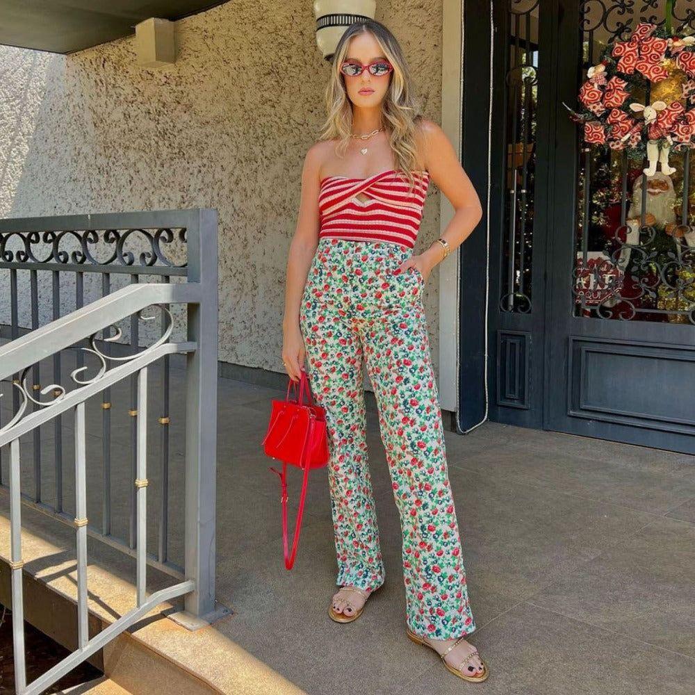 Woman in a striped top and floral pants holding a red handbag on a porch.