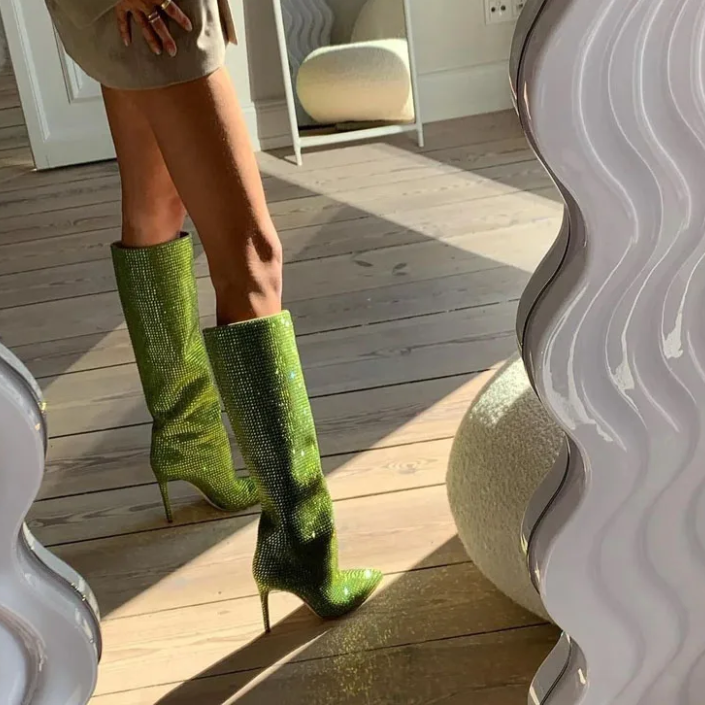 Green textured high-heeled boots worn indoors on a wooden floor.