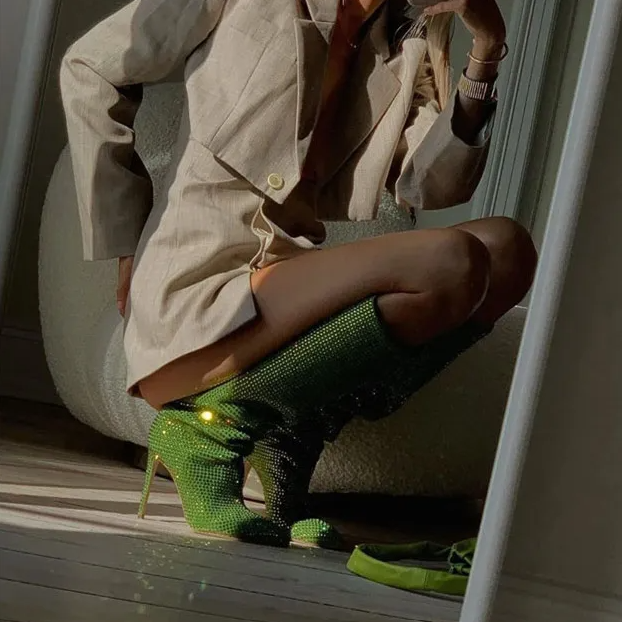 Person wearing a beige trench coat and green high-heeled shoes on a wooden floor.