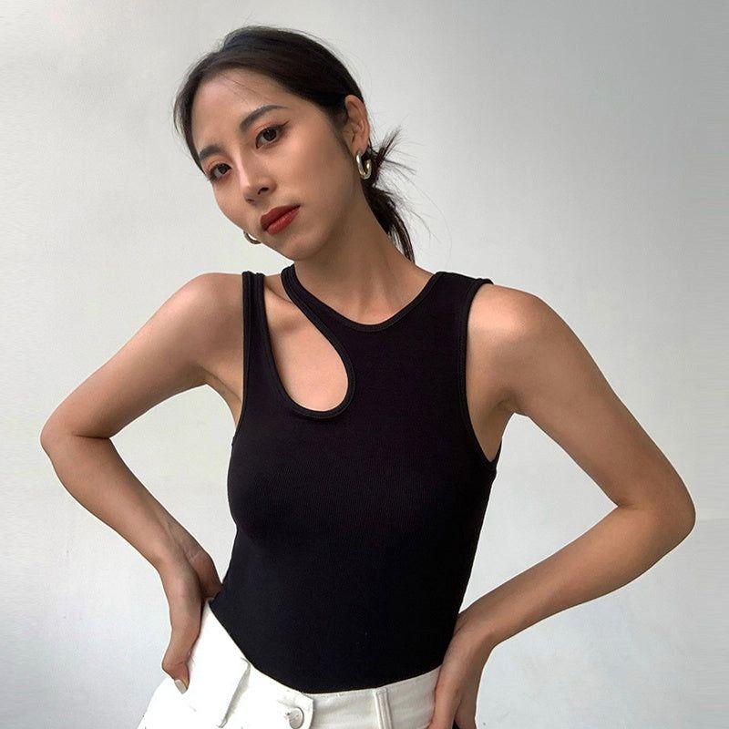 Woman wearing a black tank top and white pants against a plain background