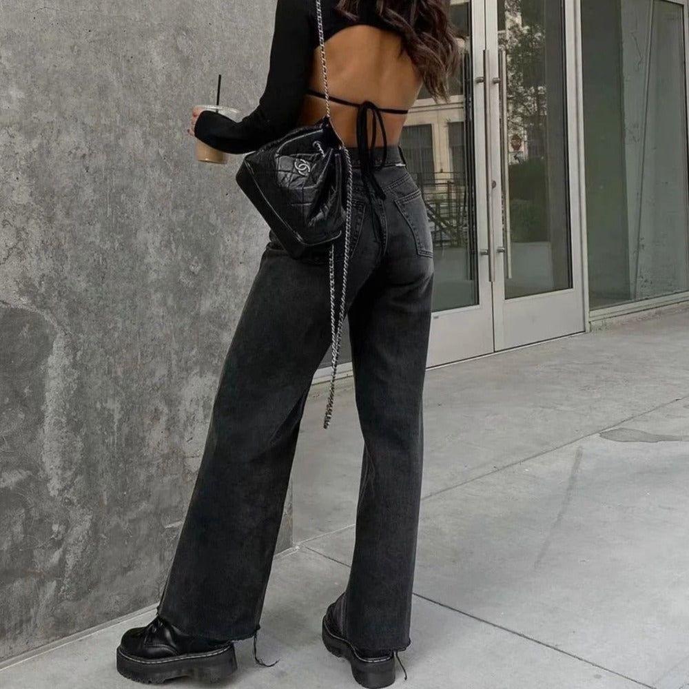 Person wearing black high-waisted jeans and platform shoes, standing against a gray wall.