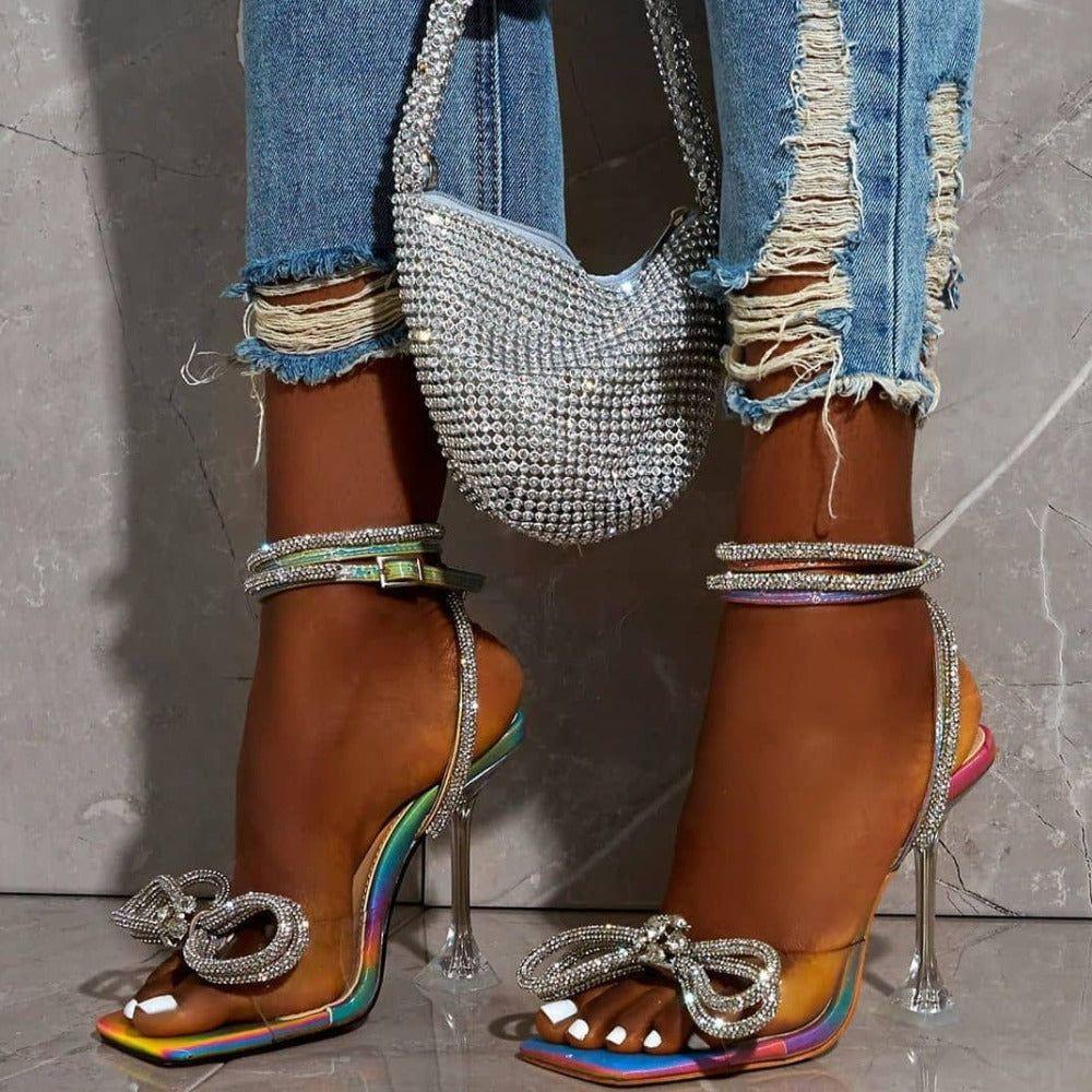 Multicolor high-heeled sandals with decorative straps and rainbow accents, paired with ripped jeans and a rhinestone handbag.