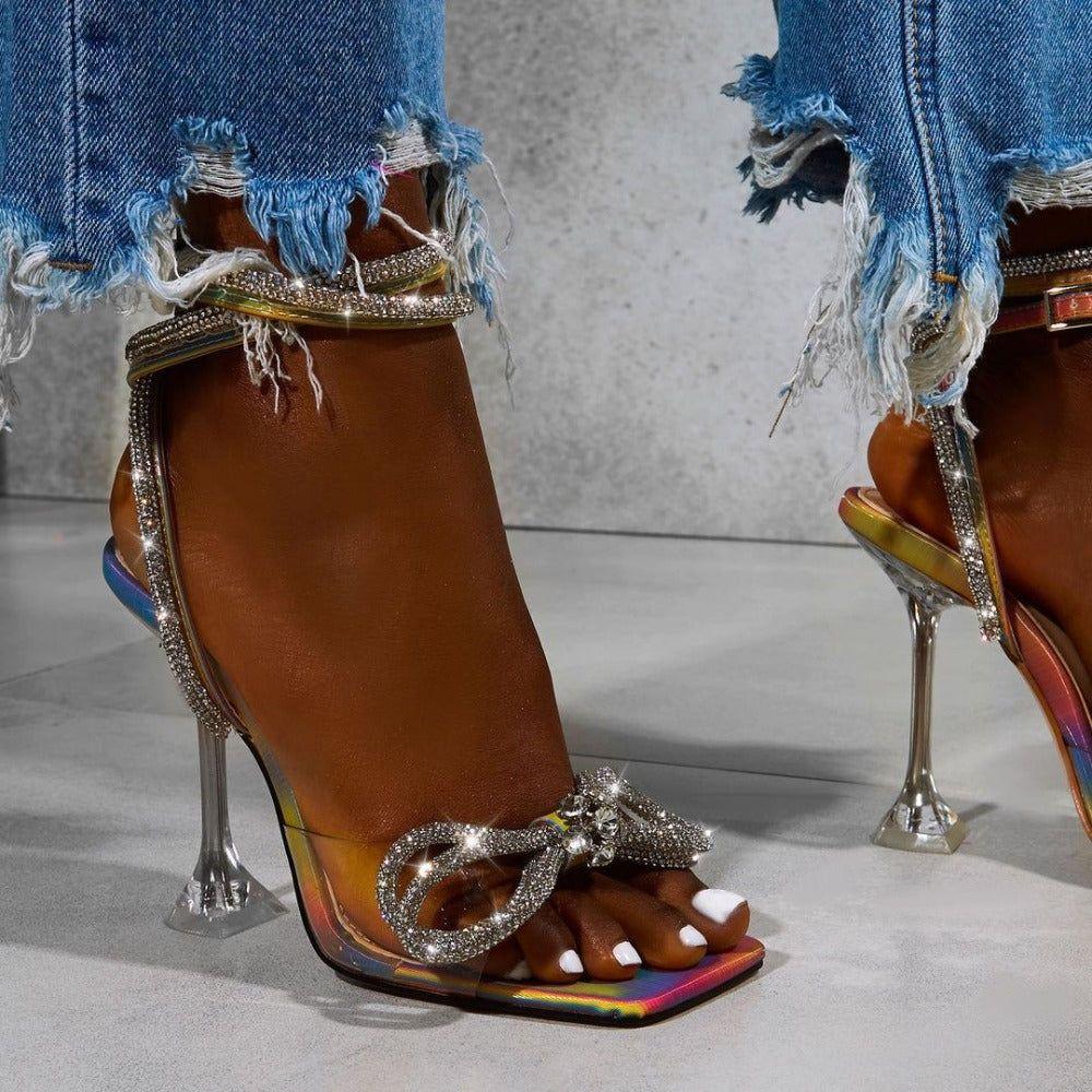 Multicolor  high-heeled sandals with decorative buckles and rhinestones, worn with ripped jeans.