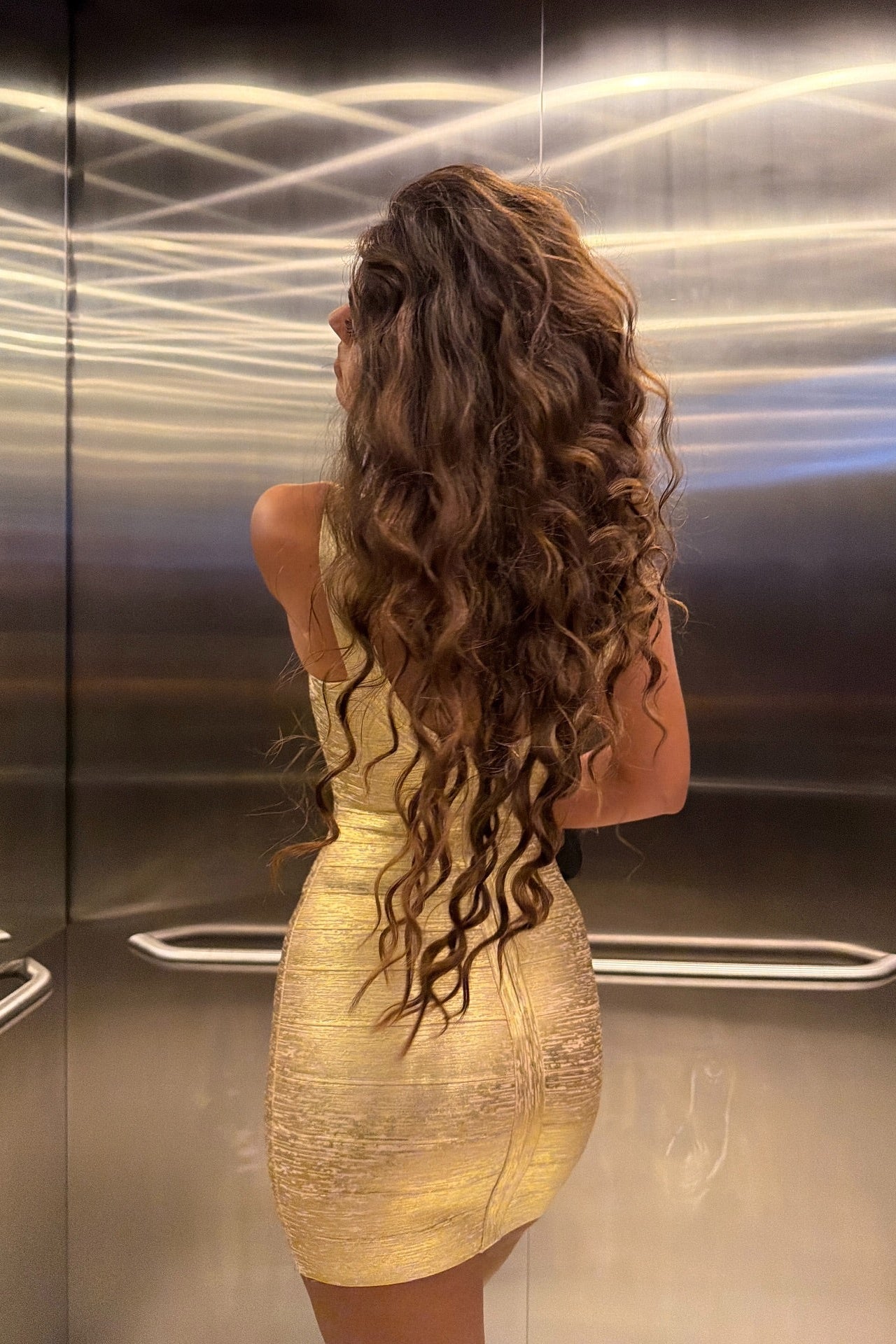 Model in gold metallic bandage mini dress, full-length front view