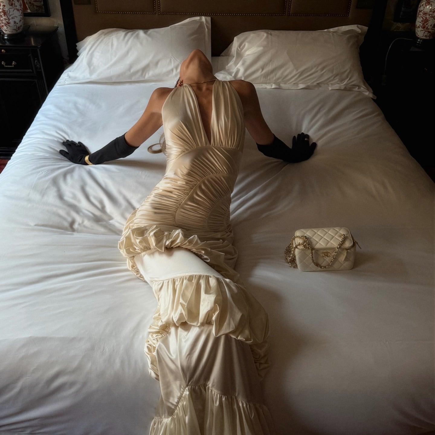 Woman in a beige dress lying on a bed with a suitcase next to her.