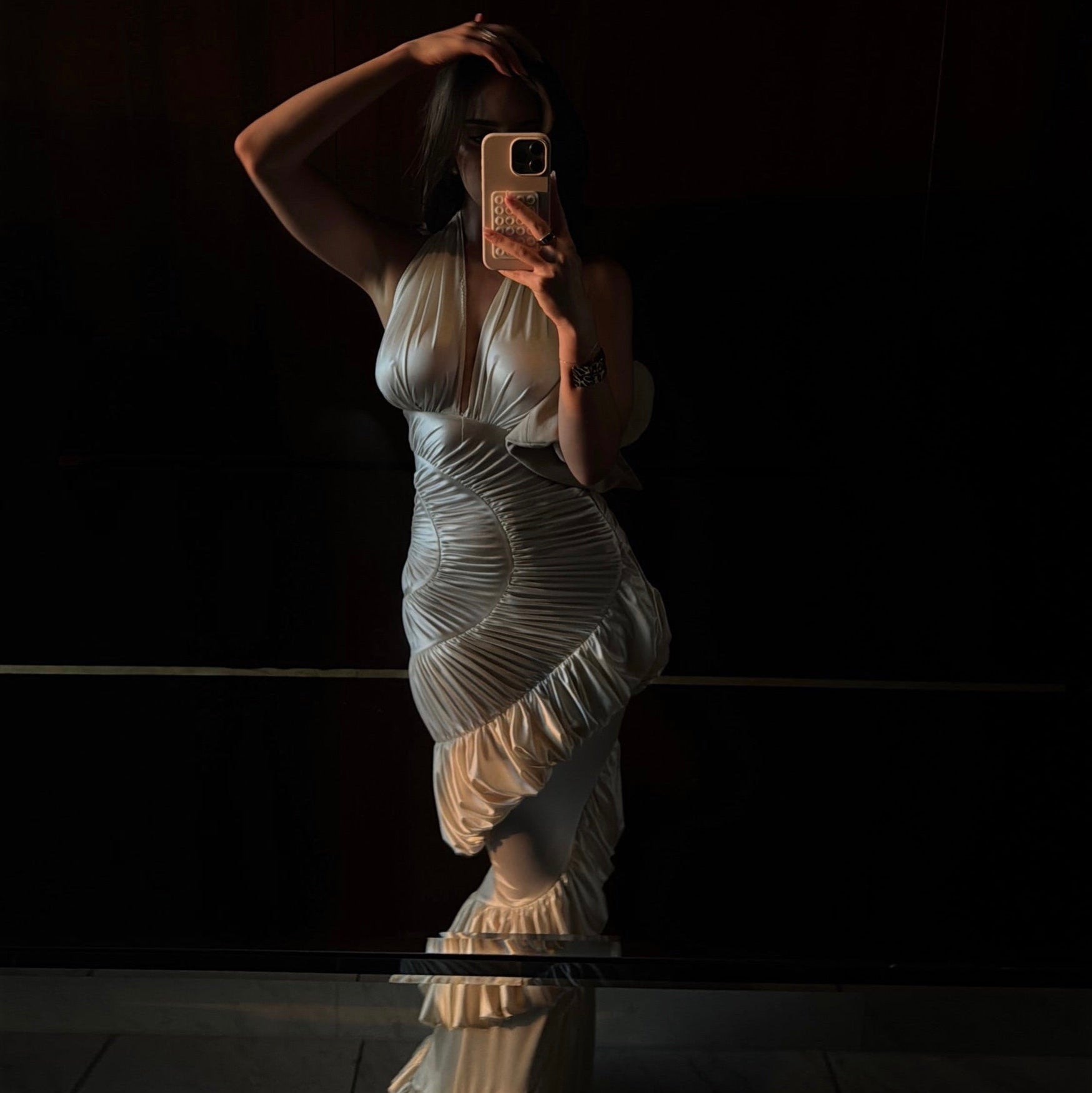 Woman in a white dress taking a mirror selfie against a dark background