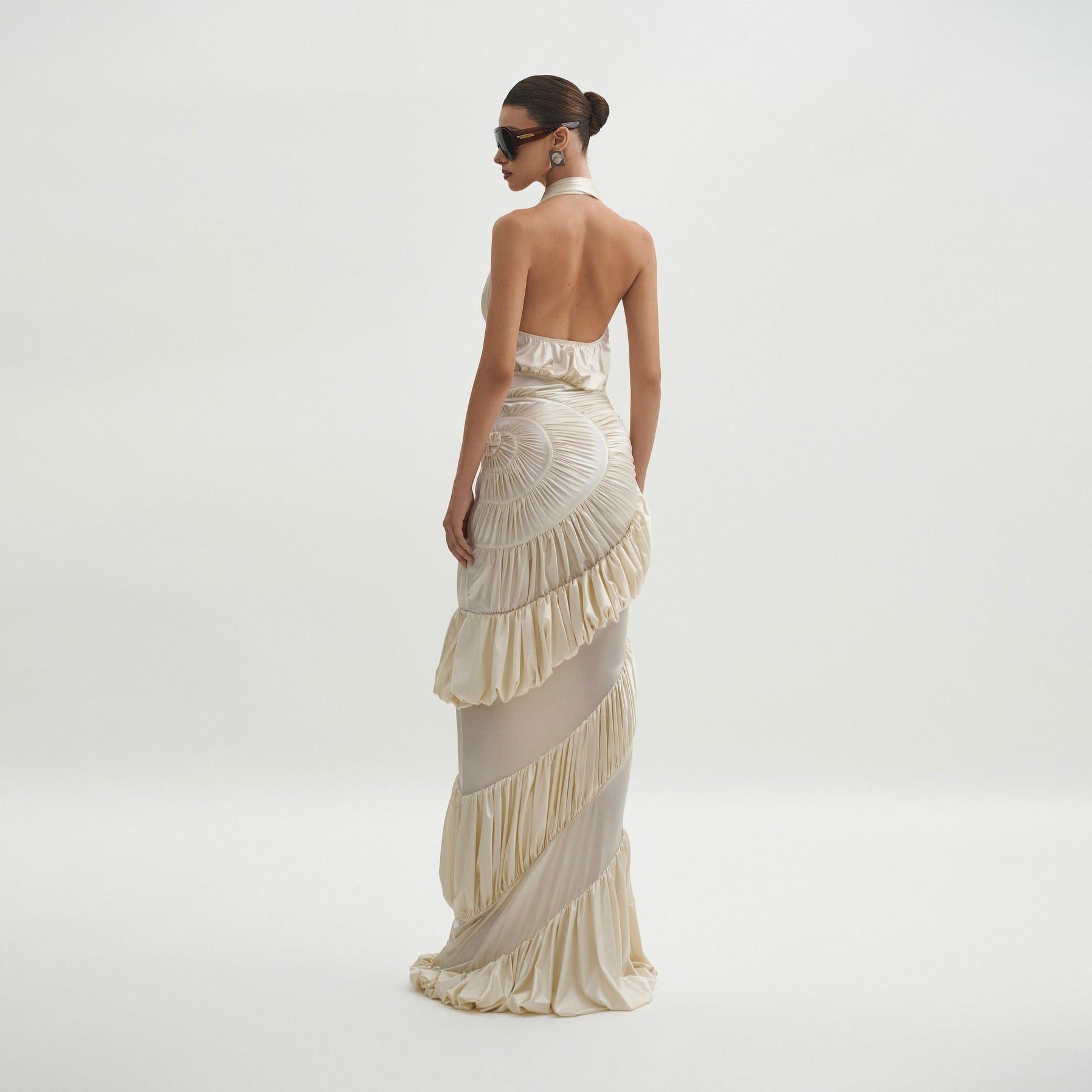 Woman wearing a long, elegant dress with ruffled layers on a plain background