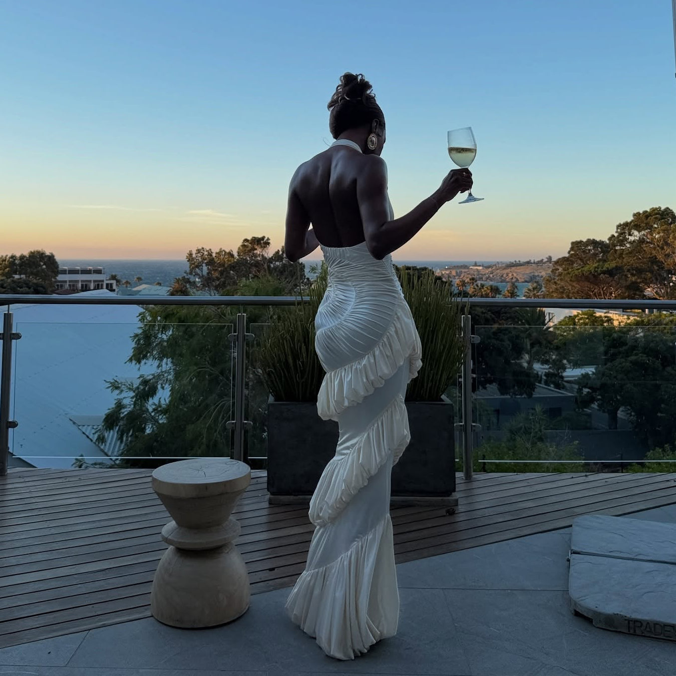 Woman in a white dress holding a glass of wine on a balcony with a scenic view.