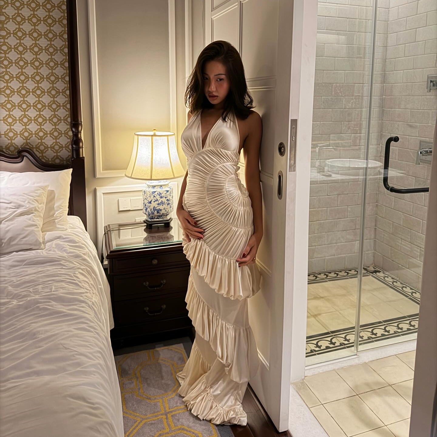 Woman in a white dress standing in a bedroom with a bathroom visible.