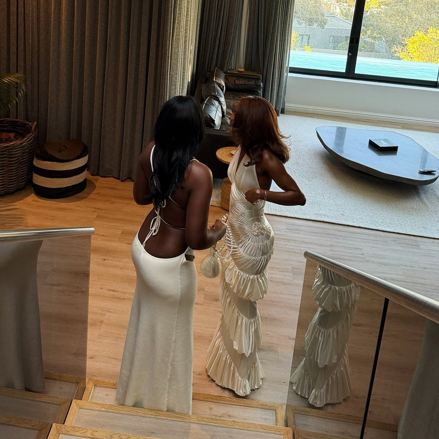 Two women in white dresses standing in a modern room with large windows.