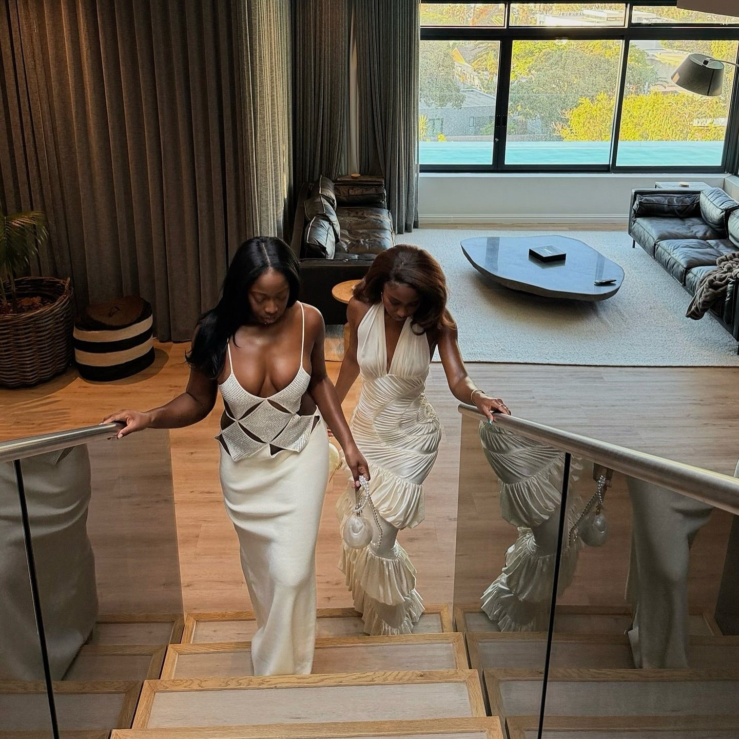 Two women in elegant dresses walking down a staircase in a modern home.