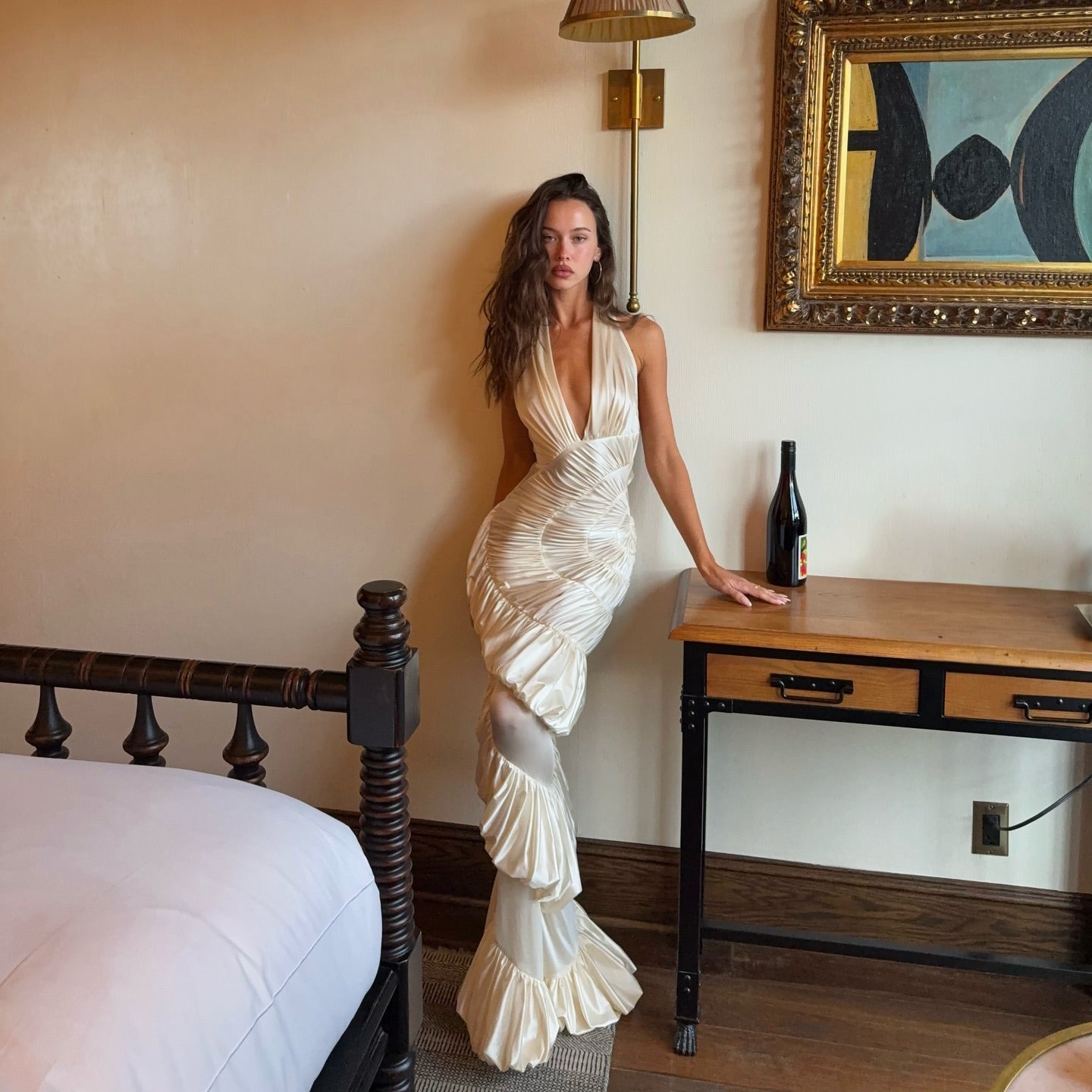 Woman in a white dress standing in a bedroom with a bed and desk.