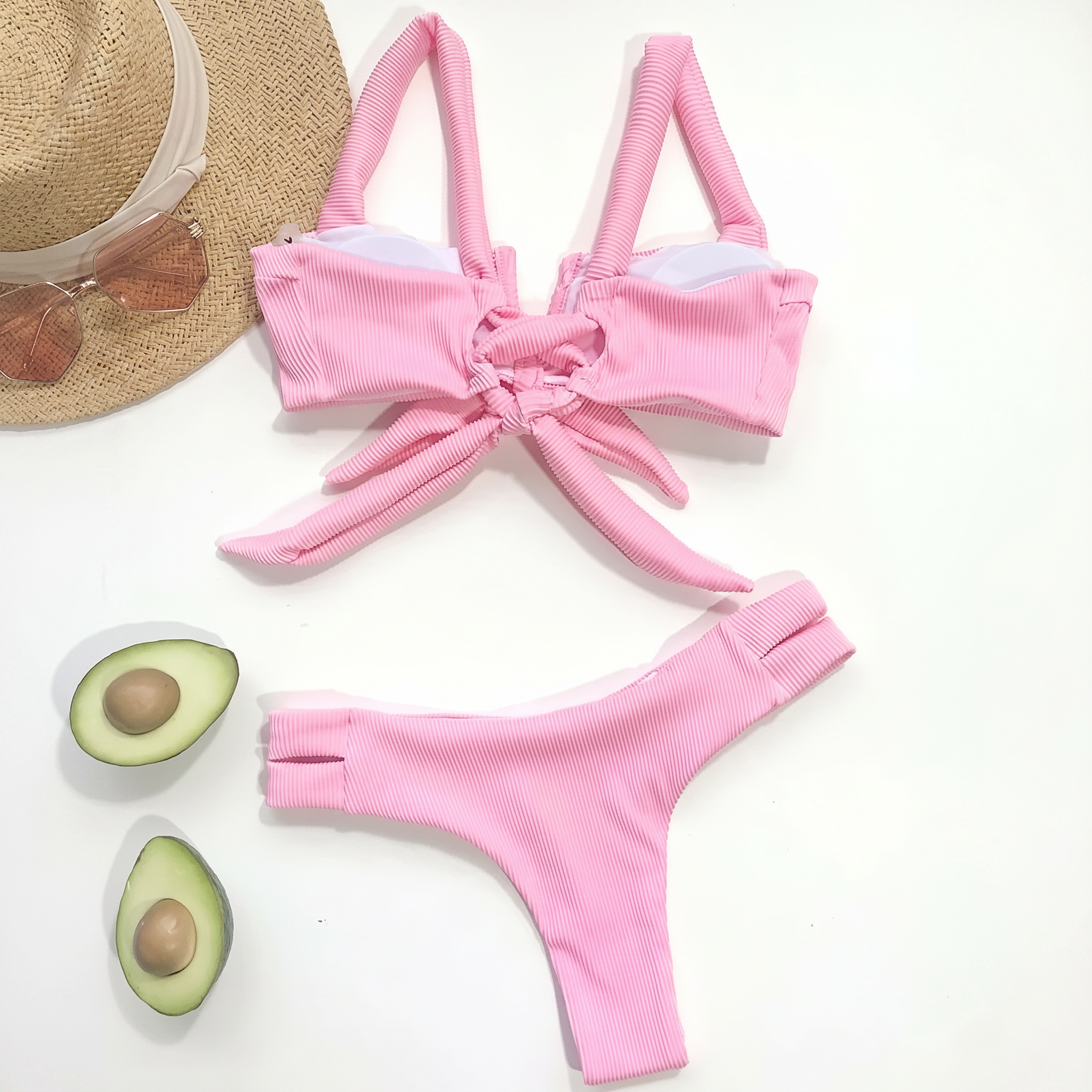 Pink bikini set with a straw hat and avocados on a white background