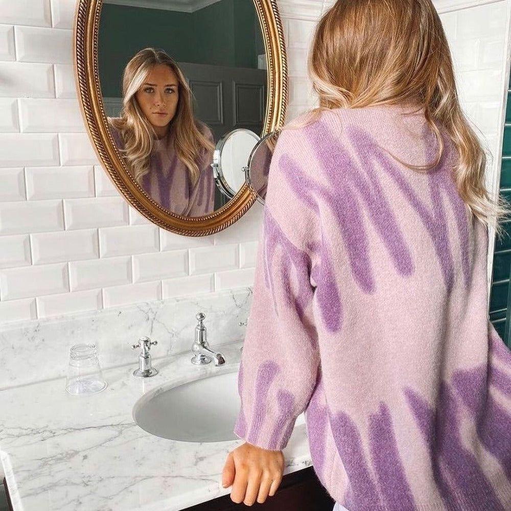 Woman wearing a purple tie-dye sweater looking at herself in the mirror.