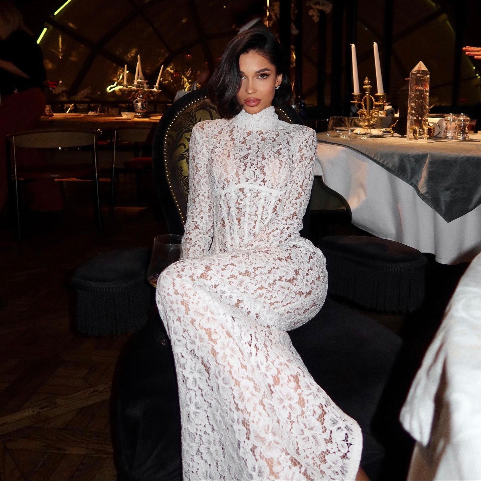 Woman in a white lace dress sitting in a dimly lit restaurant.