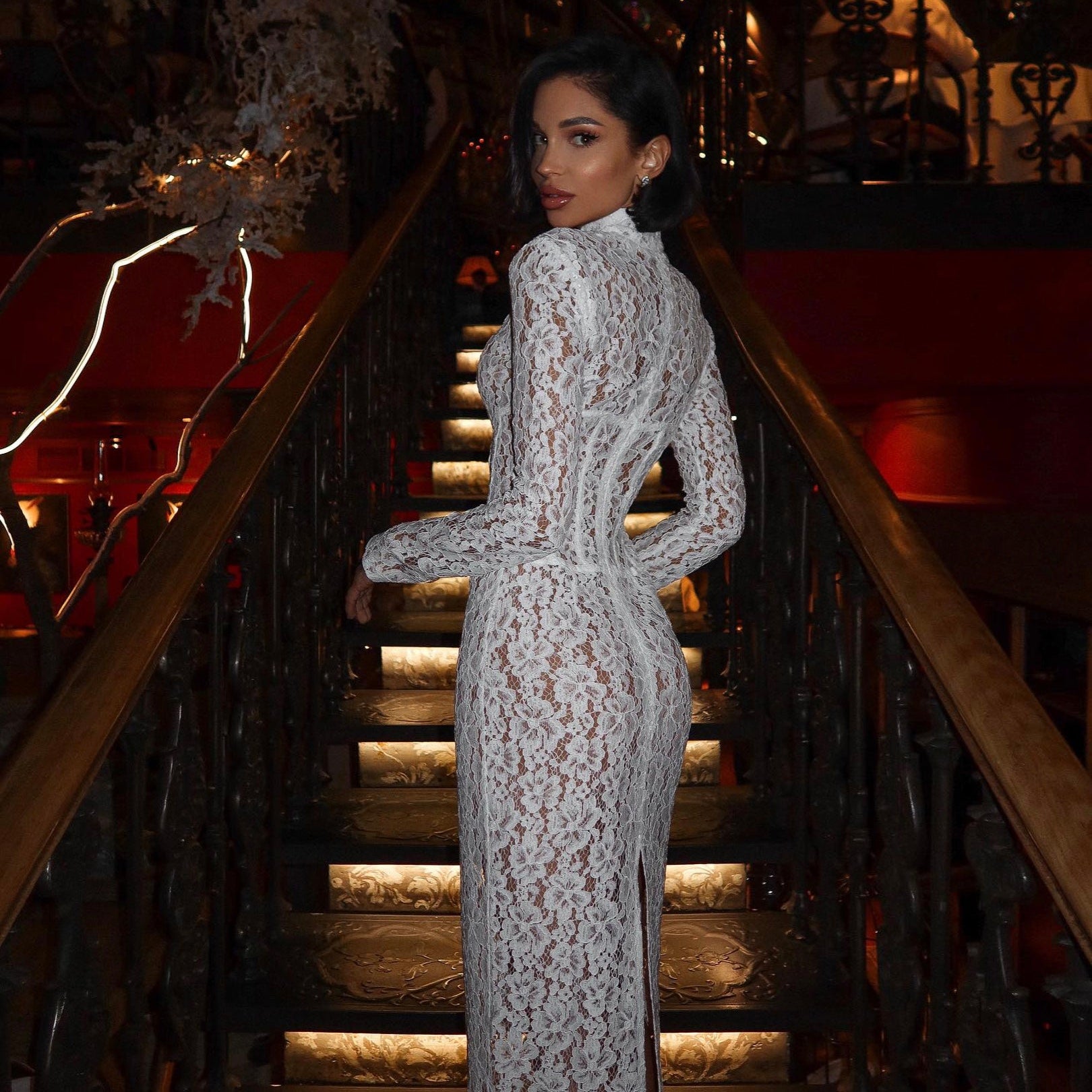Woman in a white lace dress standing on a staircase in an elegant setting