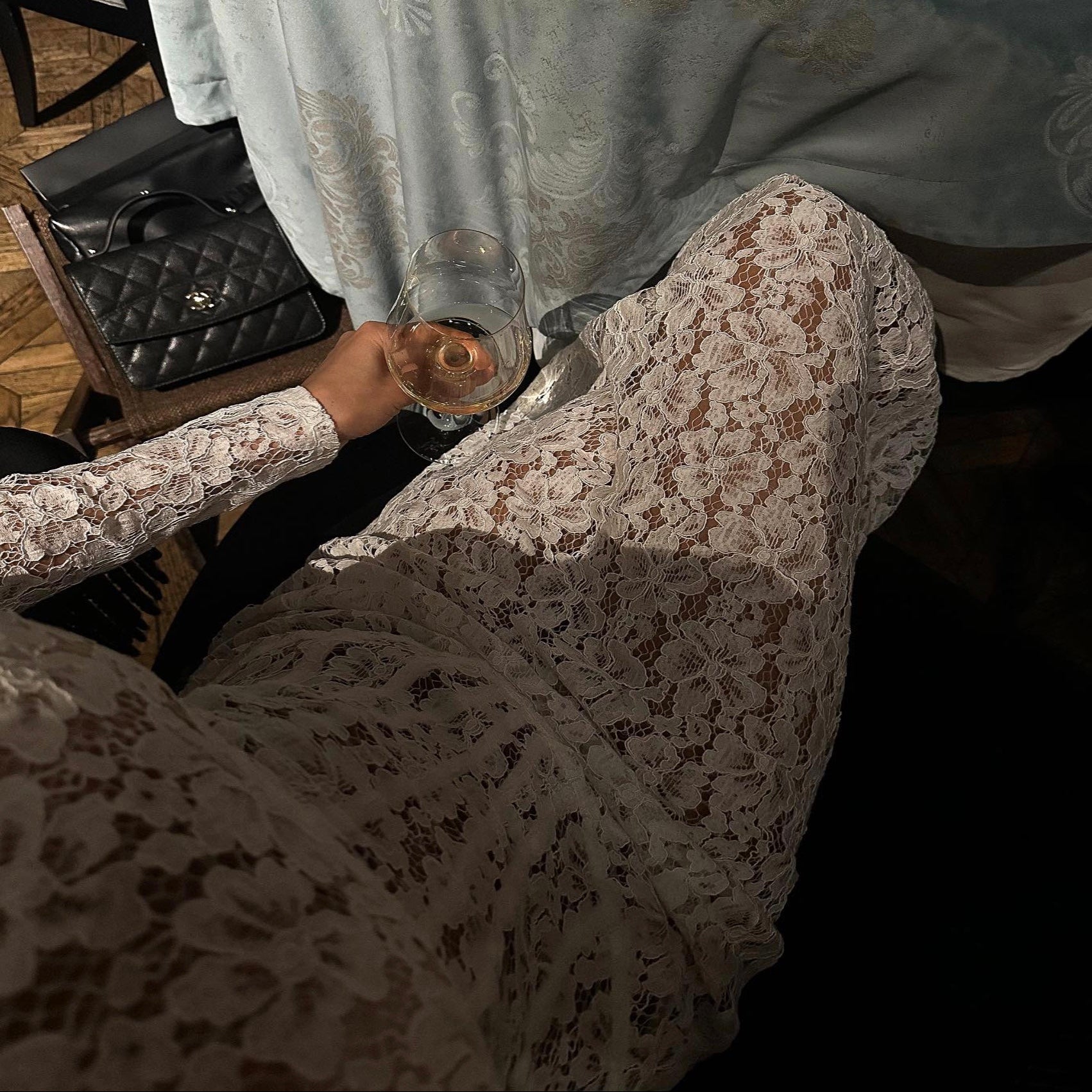Person wearing a lace dress holding a glass with a blurred background
