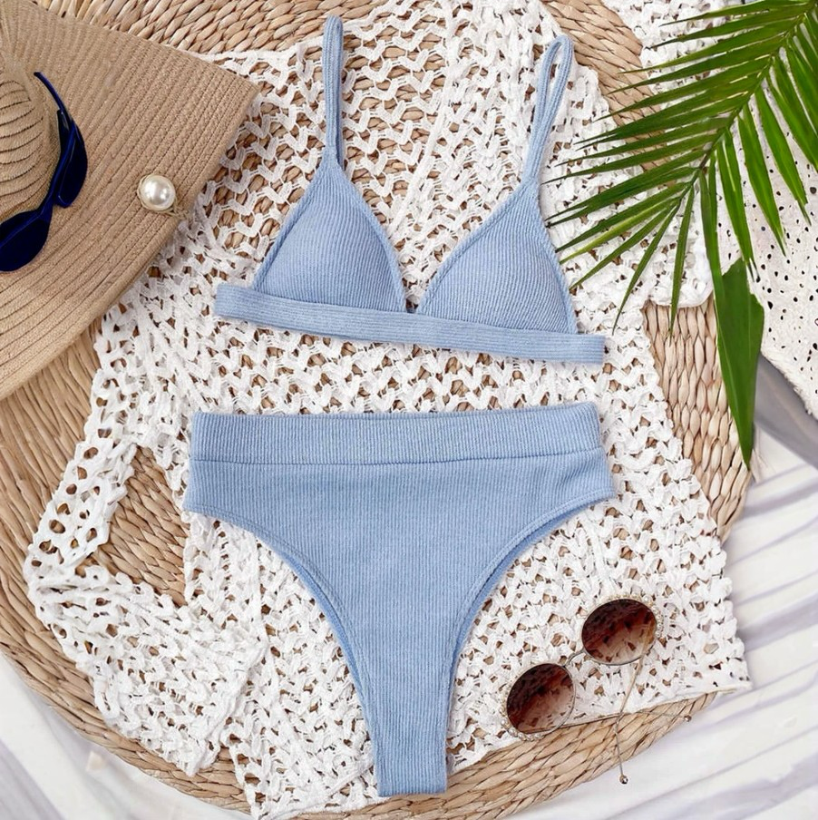Blue bikini set on a textured surface with sunglasses and a hat.