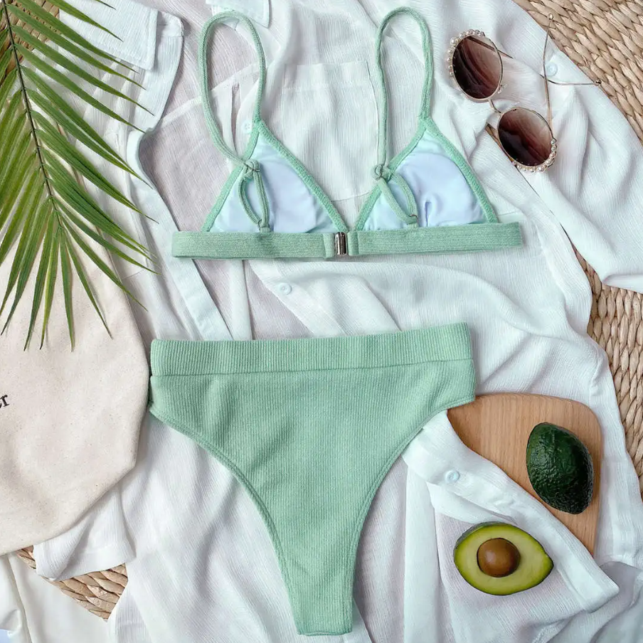 Green bikini set with sunglasses and avocado on a white surface
