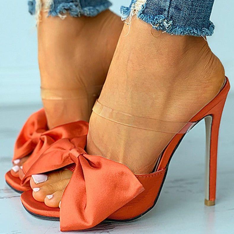 Orange high-heeled shoes with bow details worn with denim jeans.