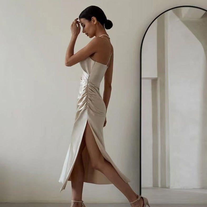 Woman in a beige dress standing in front of a mirror in a minimalistic room.