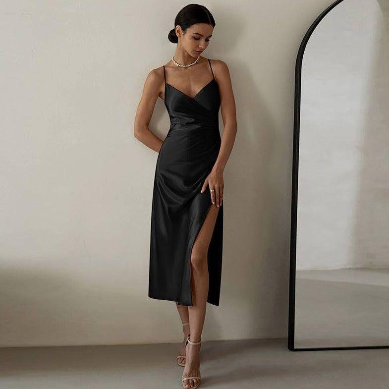 Woman in a black satin dress standing next to a mirror against a plain wall.