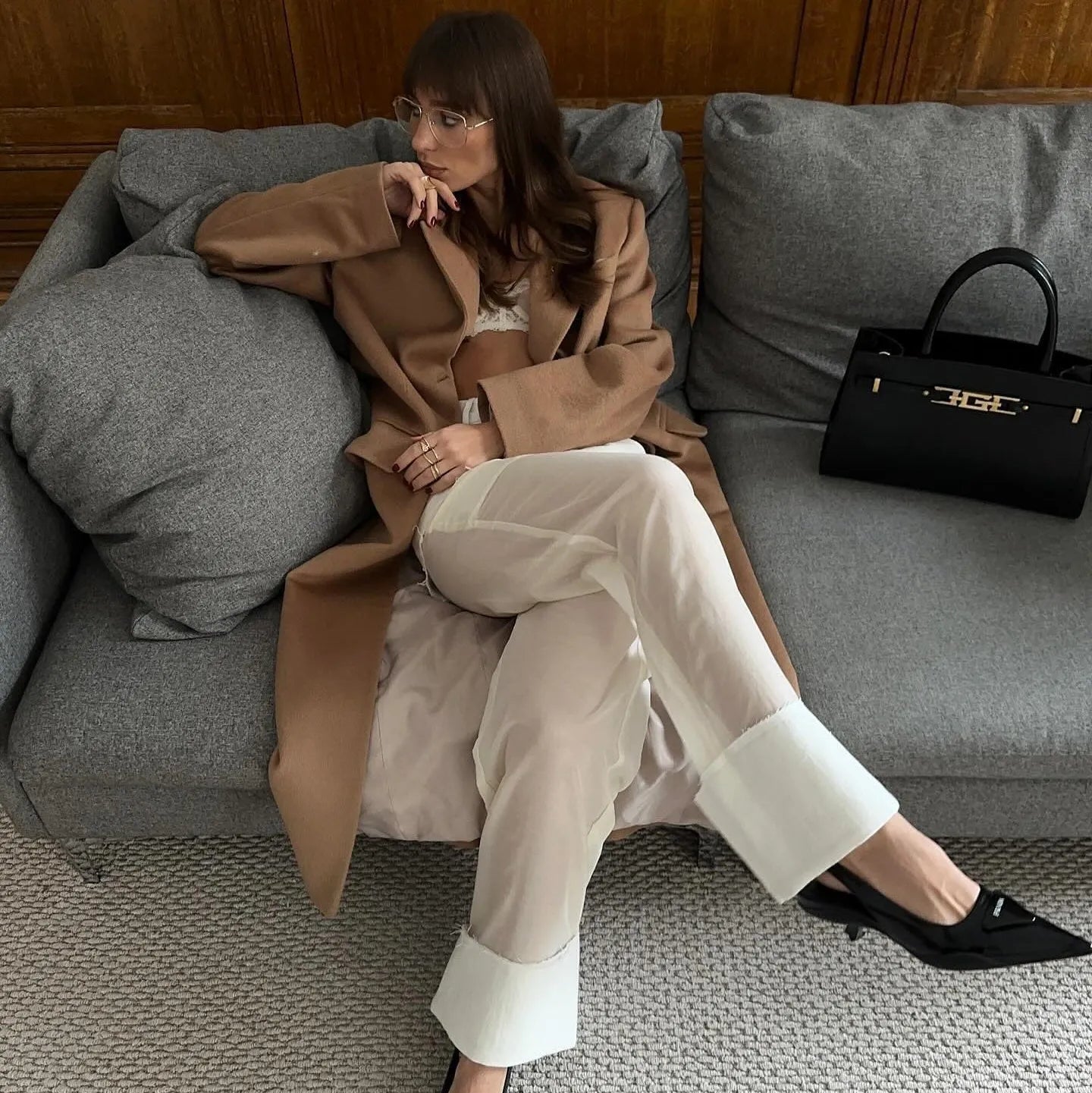 Cropped coat with sheer white pants and black handbag on a couch.