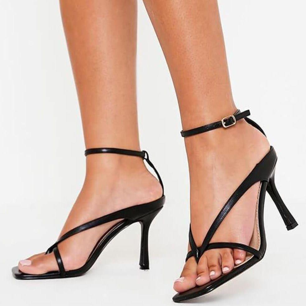 Black high-heeled sandals worn by a person on a white background