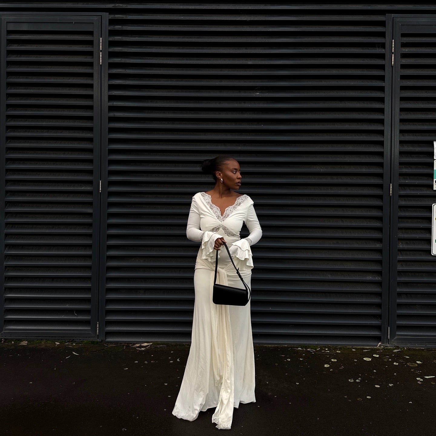 Woman in a white dress standing in front of black shutters