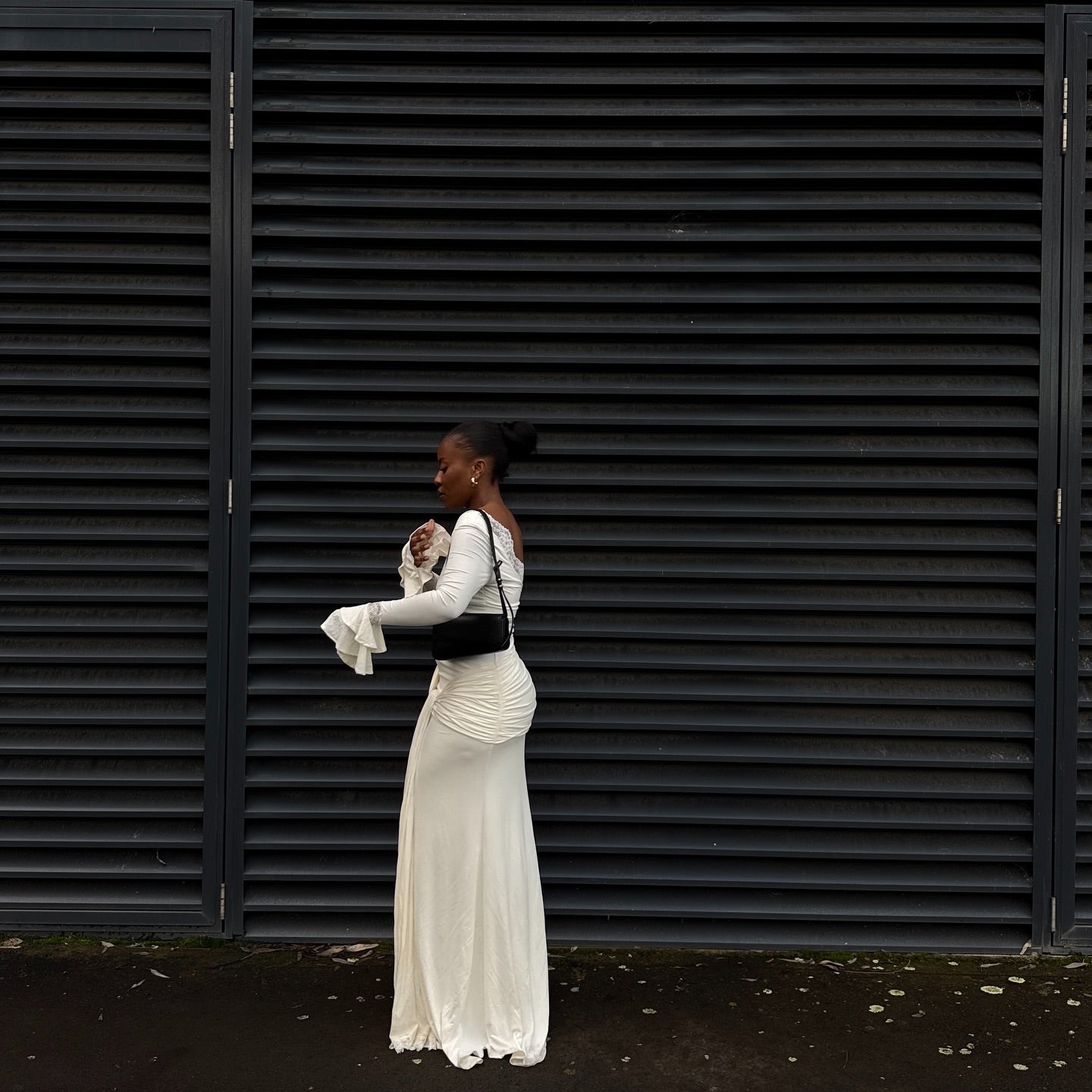 Woman in a white dress standing against a black shuttered wall