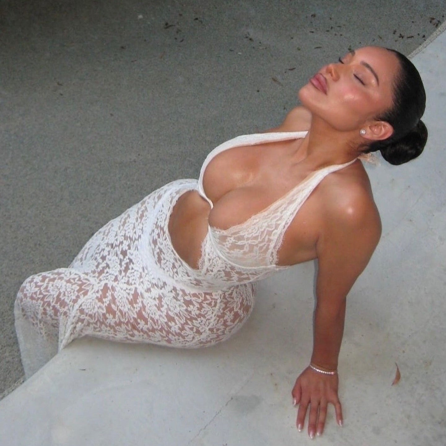 Woman in a white lace dress lying on a concrete surface.