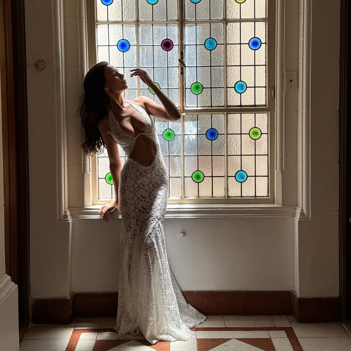 Woman in a white dress standing in front of a stained glass window with colorful circles.